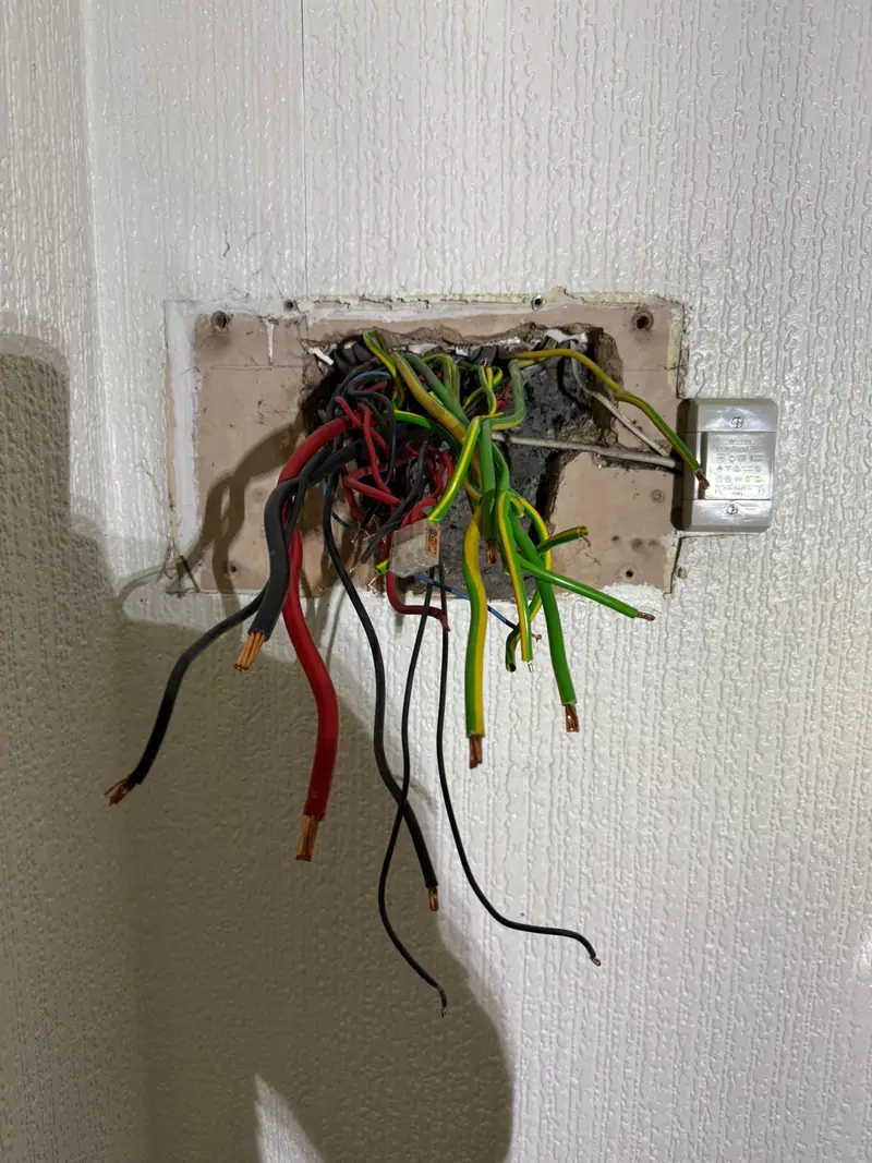 Old red and black wiring hanging from the wall where the previous fuse box was removed
