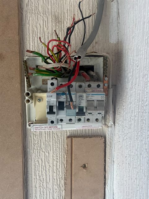 An ageing consumer unit with the cover off, wired in the old red and black colours, before we replaced it.